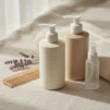 Unlabelled shampoo, conditioner and leave-in mist bottles on cream linen with a wooden wide-tooth comb and a folded towel