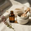 Unlabelled exfoliating serum bottle and a jar of fine face scrub on cream linen with a muslin cloth and dried plum flowers