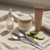 Unlabelled eye care products on cream linen with chilled spoons and cucumber slices for reducing puffy eyes