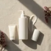 Unlabelled sunscreen bottle, tube and stick on cream linen in soft sunlight with a lotion swatch and plum-coloured dried flowers