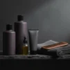Men's grooming products, a beard oil bottle and a towel on a dark bathroom shelf