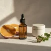 Unlabelled glass dropper serum bottle with fresh orange slices and a cream jar on a cream linen surface in soft morning light