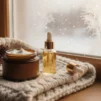 Unlabelled jar of rich face cream and a facial oil bottle on a wool knit blanket beside a frosted window